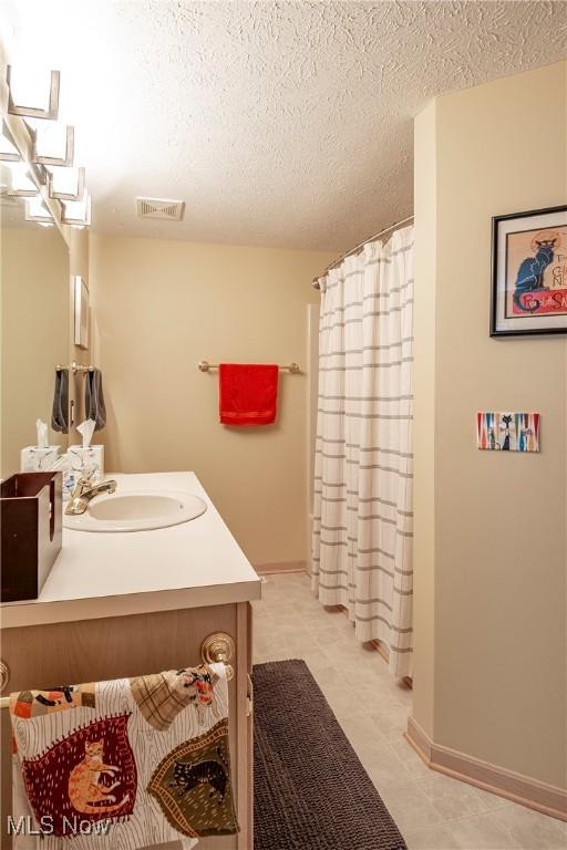 bathroom with visible vents, curtained shower, a textured ceiling, baseboards, and vanity