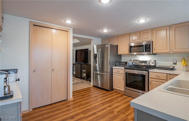 kitchen with light brown cabinetry, light countertops, light wood-type flooring, recessed lighting, and appliances with stainless steel finishes