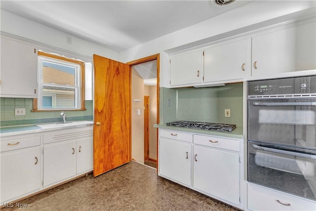 kitchen with a sink, light countertops, stainless steel gas stovetop, dobule oven black, and white cabinetry