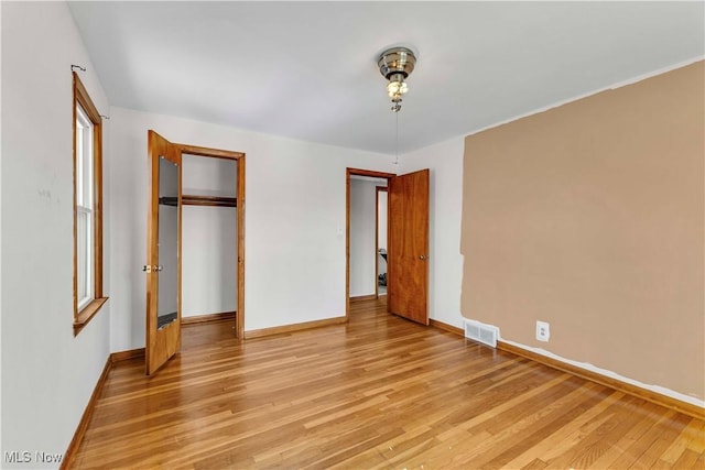 unfurnished bedroom featuring visible vents, baseboards, a closet, and light wood-style flooring