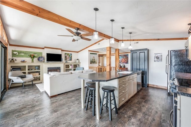 kitchen with dark countertops, vaulted ceiling with beams, appliances with stainless steel finishes, a fireplace, and a sink