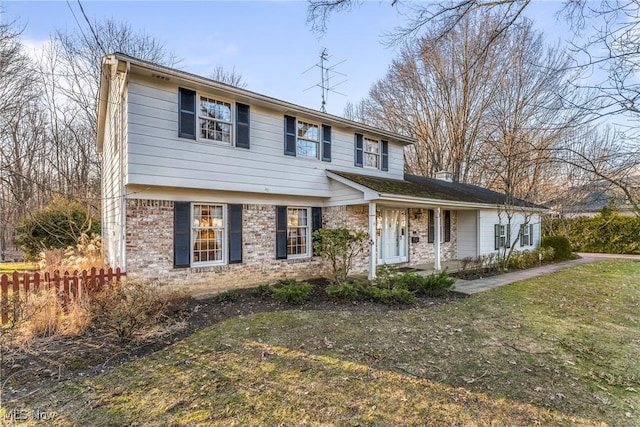 colonial home with brick siding, a front yard, and fence