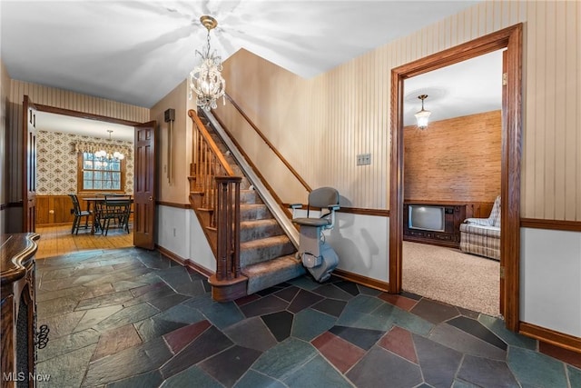 stairs featuring stone tile flooring, a notable chandelier, wallpapered walls, and baseboards