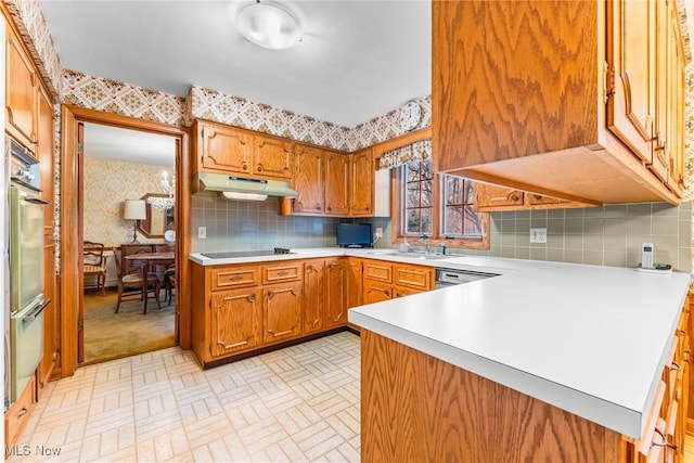 kitchen with wallpapered walls, light countertops, black electric stovetop, and under cabinet range hood