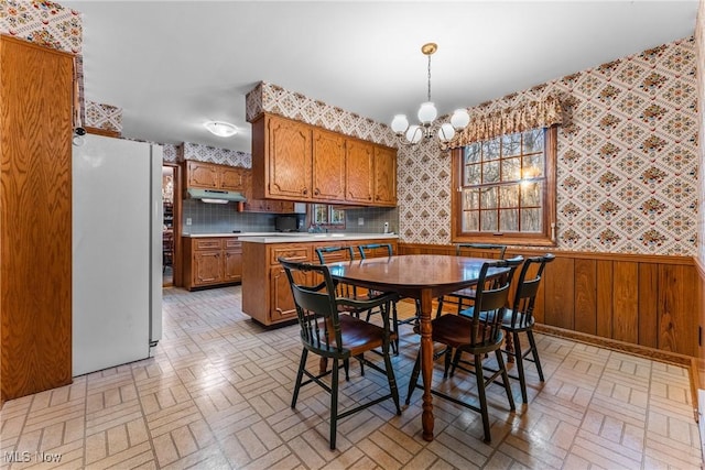 dining space with a notable chandelier, wainscoting, brick patterned floor, and wallpapered walls