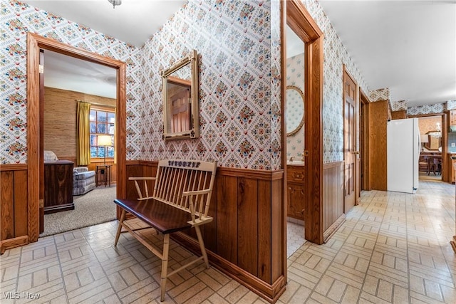 hall with a wainscoted wall, brick patterned floor, and wallpapered walls