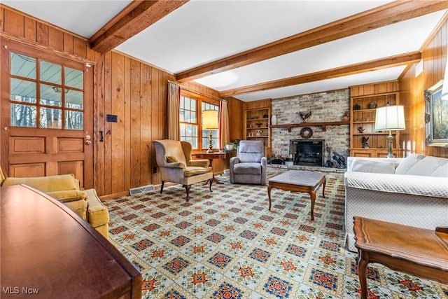 carpeted living area with wooden walls, built in shelves, baseboards, beam ceiling, and a fireplace