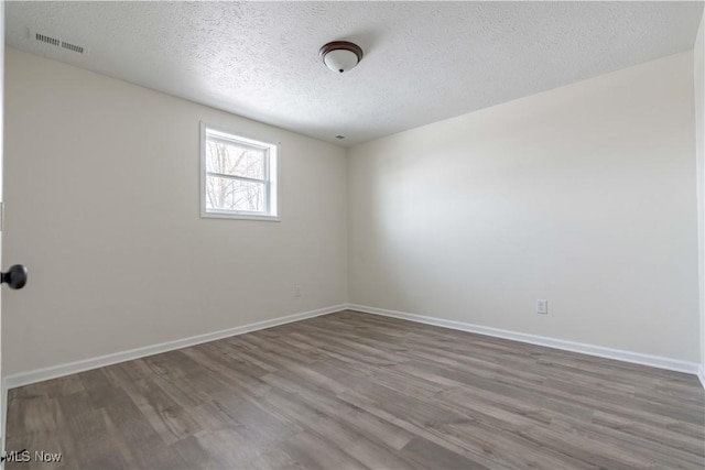 spare room featuring visible vents, a textured ceiling, baseboards, and wood finished floors