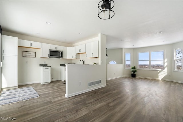 kitchen with stainless steel microwave, visible vents, wood finished floors, and white cabinetry