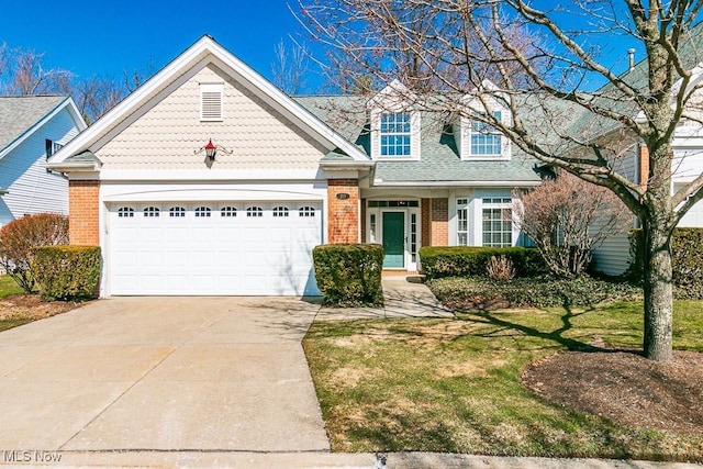 view of front facade with a front lawn, concrete driveway, an attached garage, a shingled roof, and brick siding