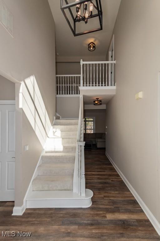 stairs featuring visible vents, wood finished floors, baseboards, and a towering ceiling