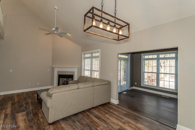 living area featuring visible vents, baseboards, high vaulted ceiling, dark wood-type flooring, and a tiled fireplace