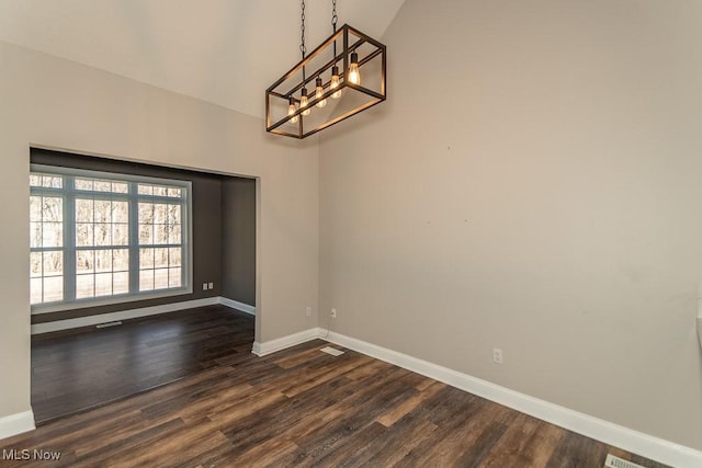 spare room with dark wood-style floors, an inviting chandelier, lofted ceiling, and baseboards