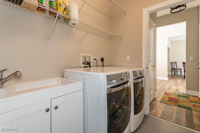 washroom featuring light wood finished floors, baseboards, separate washer and dryer, cabinet space, and a sink