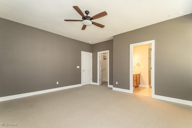 unfurnished bedroom featuring a ceiling fan, baseboards, ensuite bathroom, light carpet, and a walk in closet