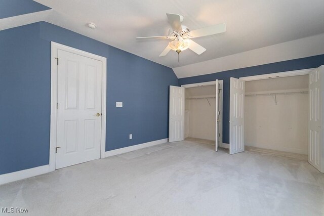 unfurnished bedroom featuring ceiling fan, baseboards, multiple closets, vaulted ceiling, and carpet flooring