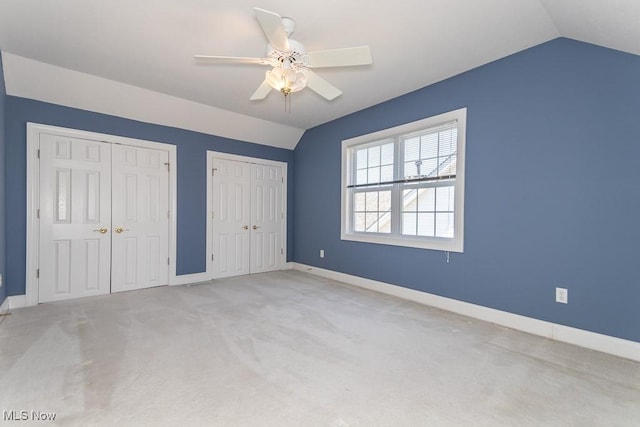 unfurnished bedroom featuring vaulted ceiling, carpet flooring, baseboards, and two closets