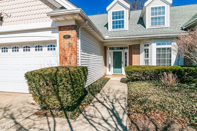 doorway to property featuring a garage, brick siding, and a shingled roof