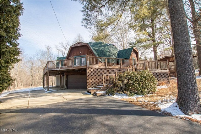 view of front of home with a garage, a gambrel roof, driveway, and a deck