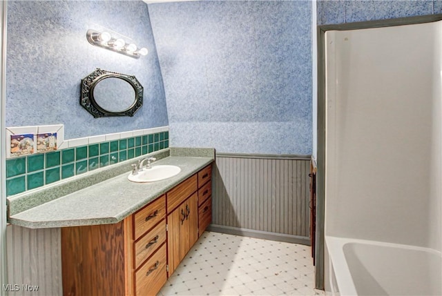 full bathroom with wallpapered walls, a wainscoted wall, a tub to relax in, tile patterned floors, and vanity