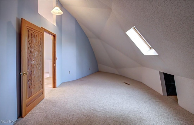 additional living space featuring vaulted ceiling with skylight, a textured ceiling, and carpet floors