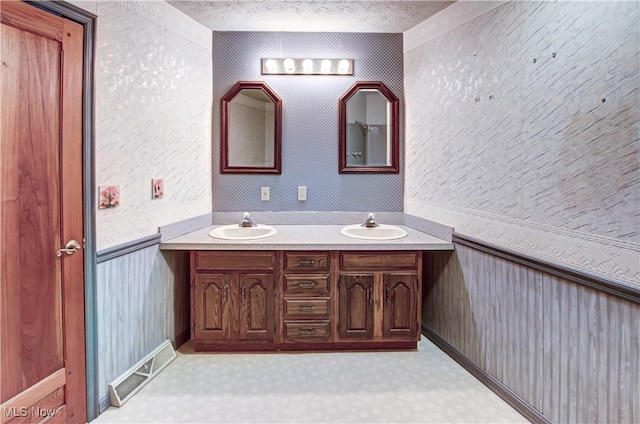 bathroom featuring a textured ceiling, double vanity, and a sink