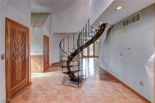 stairway featuring a textured ceiling, visible vents, wainscoting, tile patterned floors, and a textured wall