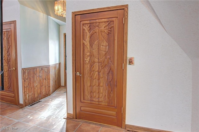 hallway with light tile patterned floors, a wainscoted wall, and wooden walls