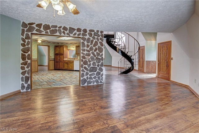 unfurnished living room featuring ceiling fan, a textured ceiling, stairs, and light wood-style floors