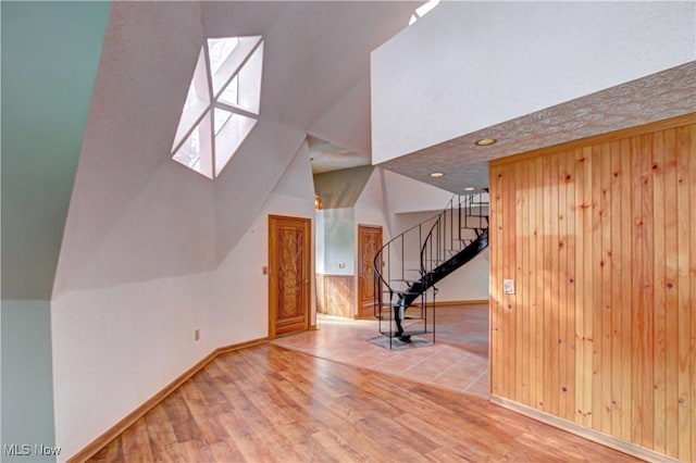 unfurnished living room with vaulted ceiling, stairs, wooden walls, and wood finished floors