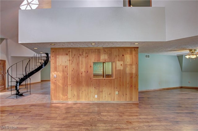 unfurnished living room with stairway, visible vents, a towering ceiling, and wood finished floors