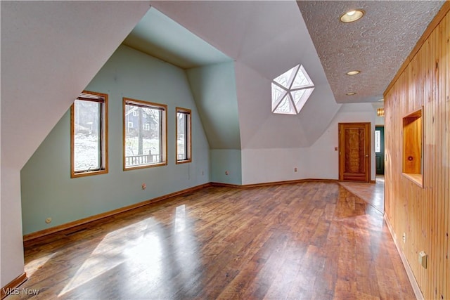 additional living space featuring light wood finished floors, a textured ceiling, baseboards, and vaulted ceiling