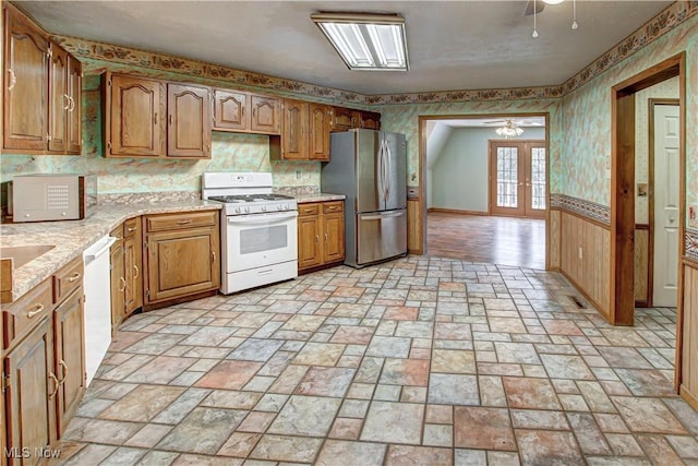 kitchen featuring a wainscoted wall, french doors, white appliances, brown cabinetry, and wallpapered walls