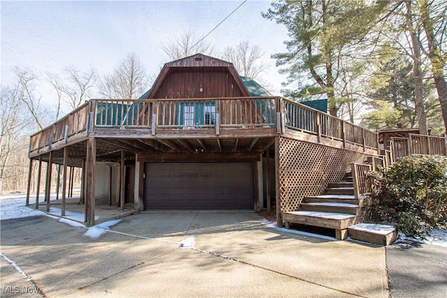 view of front of home featuring a gambrel roof, concrete driveway, an attached garage, a wooden deck, and stairs