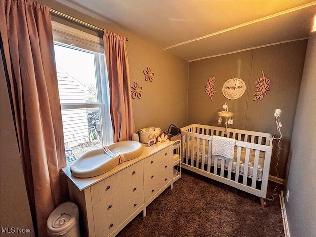 bedroom featuring a nursery area and dark carpet