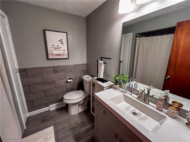 bathroom featuring toilet, a textured ceiling, wood finished floors, tile walls, and vanity