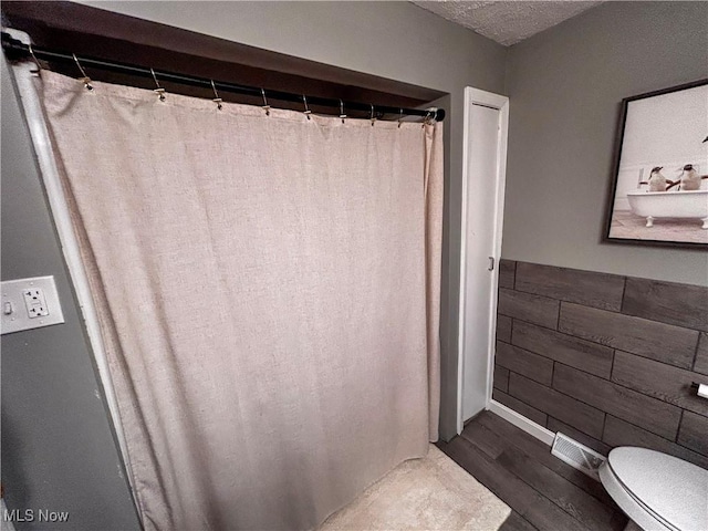 bathroom with a shower with curtain, wood finished floors, a wainscoted wall, a textured ceiling, and toilet