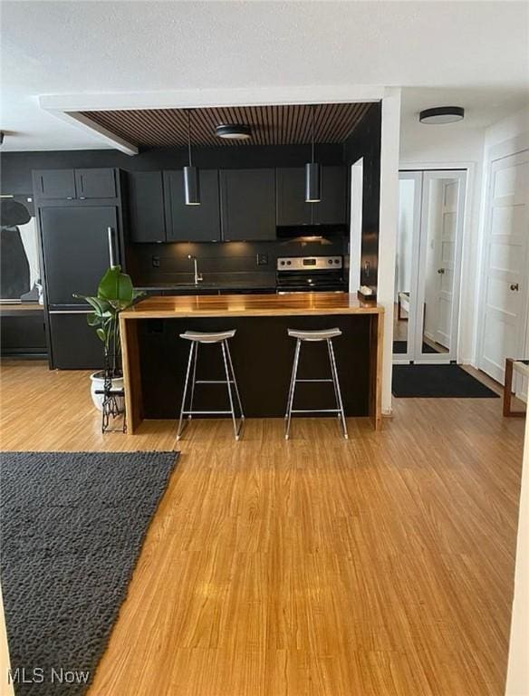 kitchen with paneled refrigerator, light wood-style flooring, a sink, stainless steel range with electric cooktop, and wooden counters