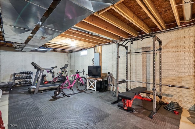 workout room featuring electric panel and brick wall