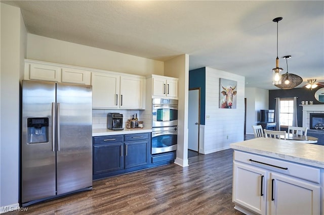 kitchen featuring dark wood-style flooring, light countertops, appliances with stainless steel finishes, white cabinetry, and decorative light fixtures