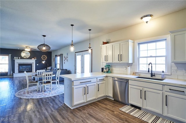 kitchen with a sink, stainless steel dishwasher, open floor plan, a glass covered fireplace, and a peninsula