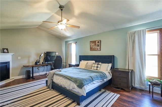 bedroom featuring baseboards, dark wood finished floors, vaulted ceiling, a fireplace, and a ceiling fan