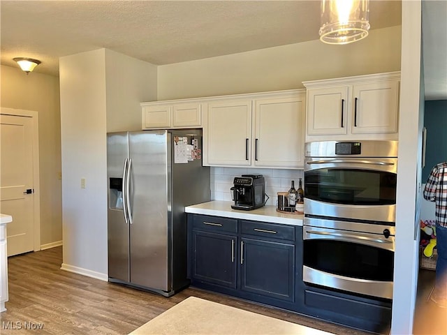 kitchen with tasteful backsplash, white cabinetry, stainless steel appliances, light wood finished floors, and light countertops