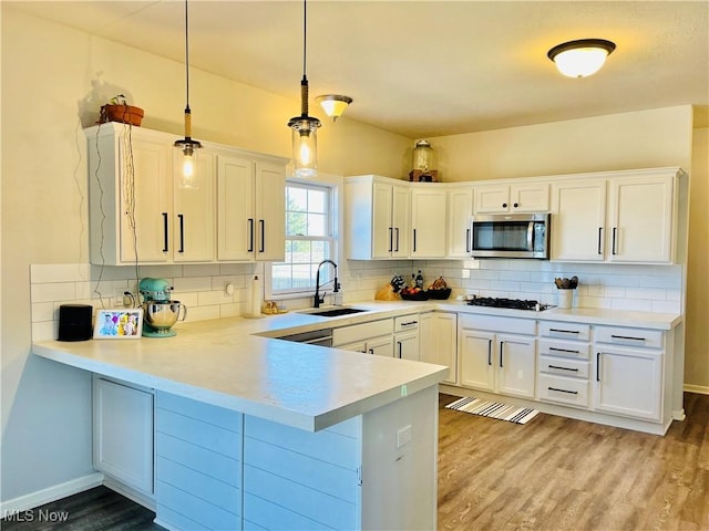 kitchen with a sink, stainless steel microwave, gas cooktop, a peninsula, and decorative backsplash