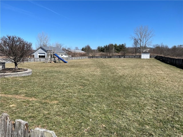 view of yard featuring a storage unit, an outbuilding, a fenced backyard, and a playground