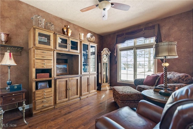 living room with a textured ceiling, ceiling fan, and dark wood-style flooring