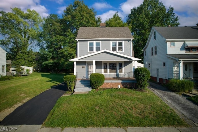 view of front of home featuring a chimney, a porch, a front yard, and a shingled roof