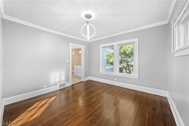 empty room featuring hardwood / wood-style flooring, baseboards, visible vents, and ornamental molding