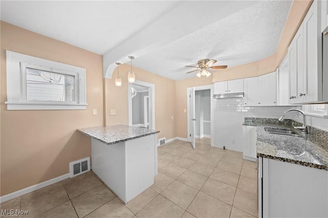 kitchen featuring visible vents, a sink, dark stone countertops, backsplash, and white cabinets