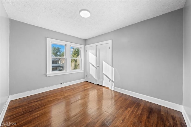 unfurnished bedroom featuring wood finished floors, baseboards, a closet, and a textured ceiling